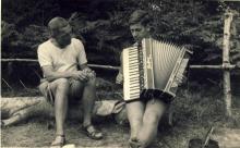 <p>c1935 - Left to right: Father George Moore, scout leader, watches George Whalley play the accordion during a scouting trip</p>